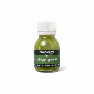 Cold-pressed green juice shot with ginger and leafy greens on a white background