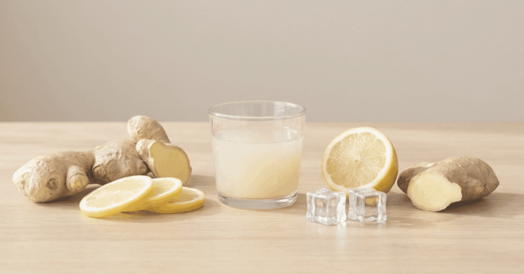 Ginger root, lemon slices and a glass of ginger lemon juice on a calm neutral background