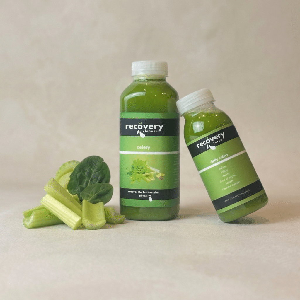 Cold-pressed celery juice bottles with fresh celery on a neutral background