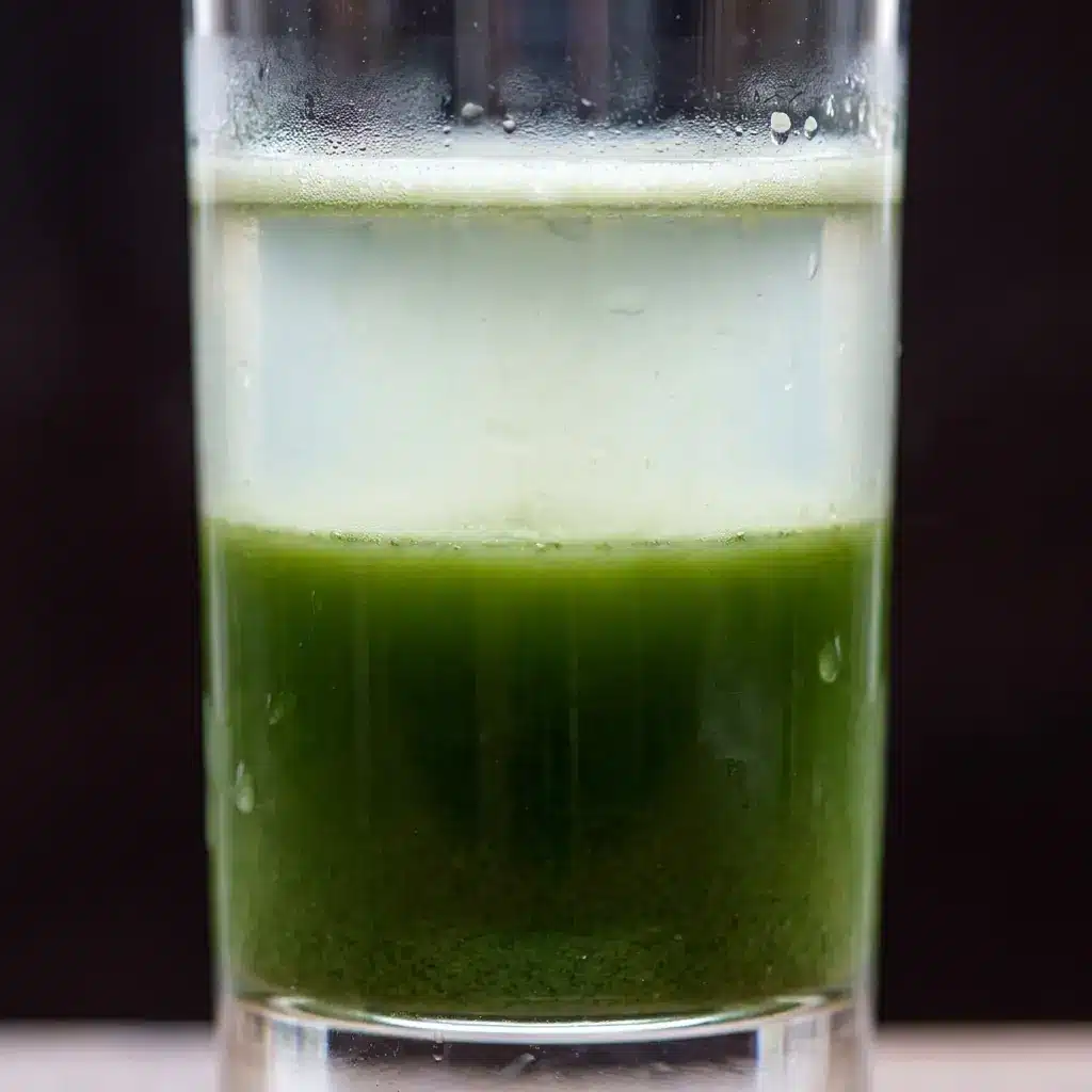 Extreme close-up of a glass of vegetable juice that has separated into layers, with foam at the top, lighter liquid in the middle and settled sediment below